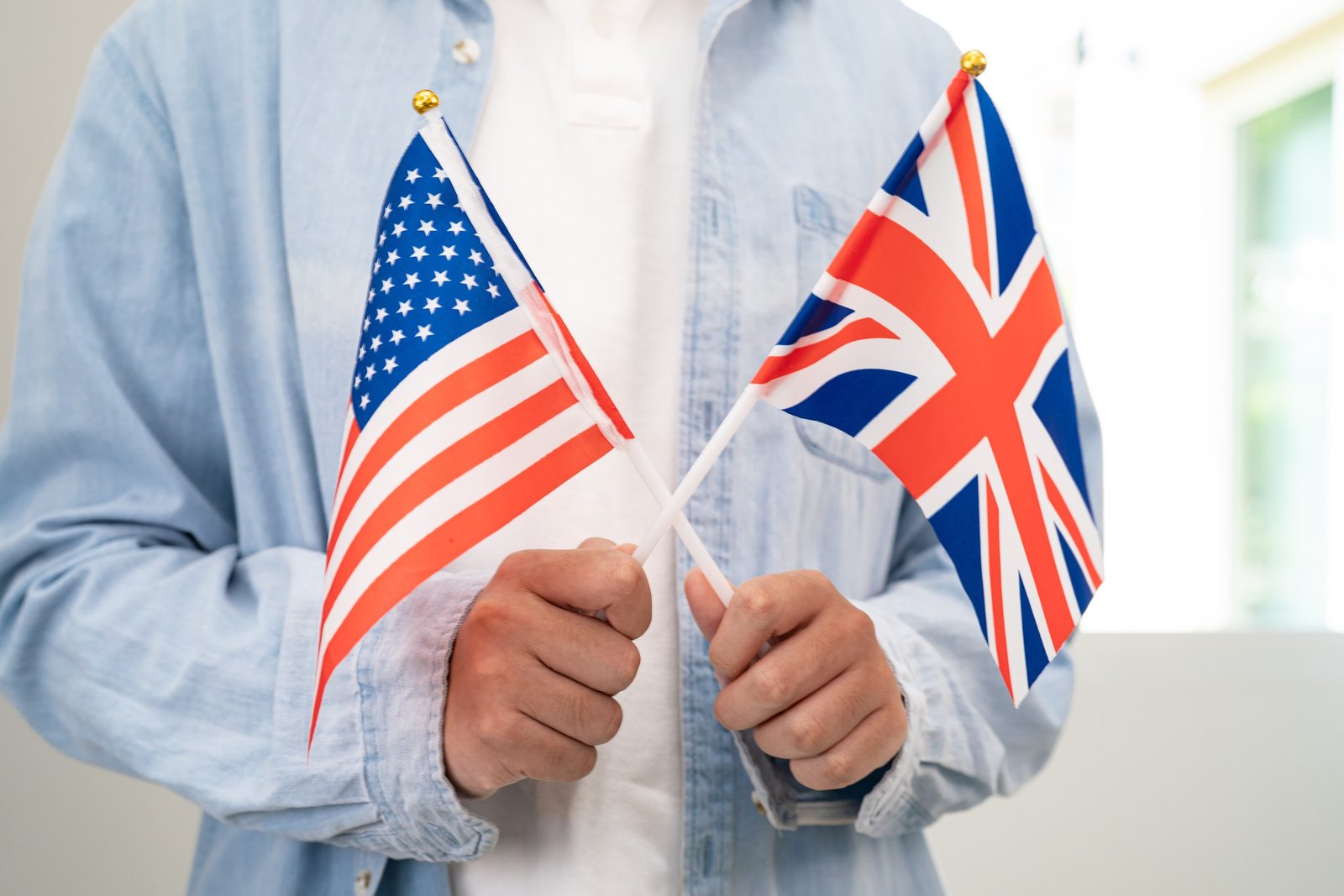 Persona sosteniendo dos banderas, la de Estados Unidos y la de Reino Unido, representando la obtención de certificados oficiales de inglés americano y británico, ideal para validar competencias lingüísticas internacionales.