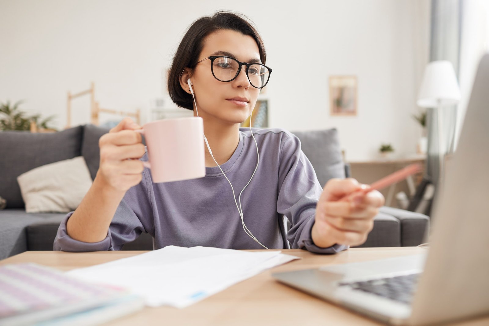 Persona participando en clase virtual de inglés, usando auriculares, tomando notas y disfrutando de una bebida, representando cómo las clases online ayudan a desarrollar tu confianza en inglés mediante un aprendizaje flexible y cómodo desde casa.
