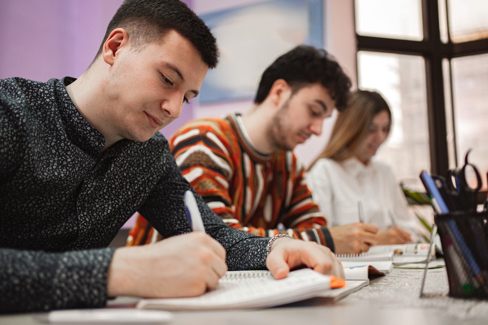 Adultos tomando notas y participando en actividades escritas durante una clase de inglés para adultos en un aula iluminada, enfocados en el aprendizaje activo y el desarrollo de habilidades lingüísticas.