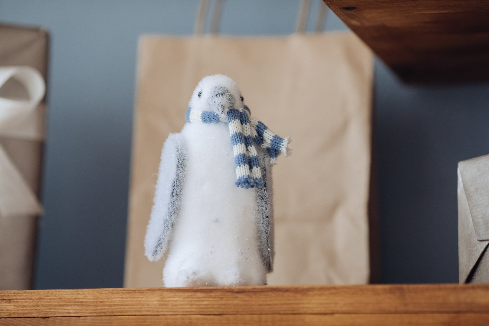 Pingüino de peluche pequeño con bufanda azul y blanca sobre una estantería, utilizado como recurso educativo en clases de inglés para infantil para estimular el aprendizaje y la participación de los niños a través de juegos y actividades temáticas.