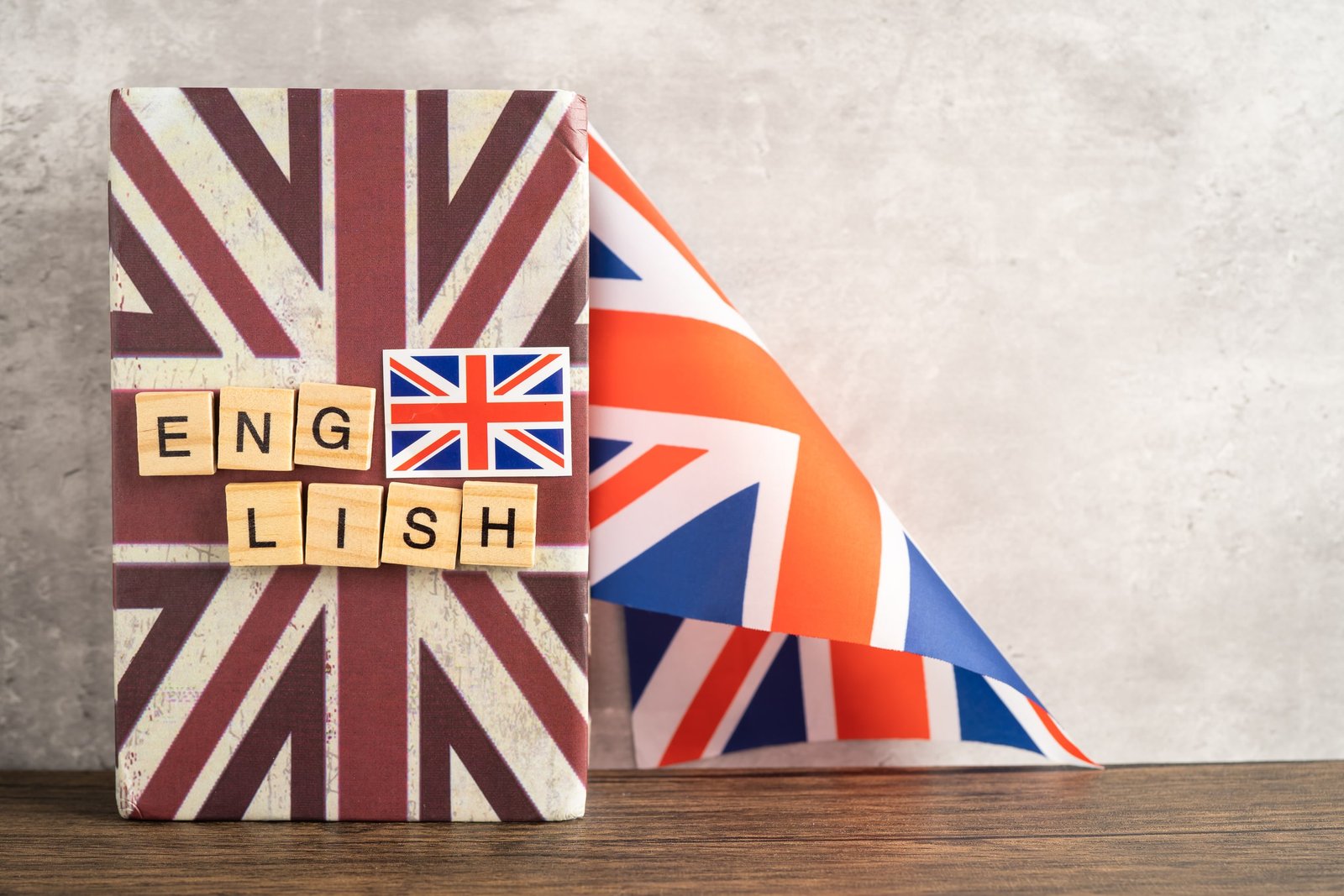 Libro decorado con la bandera del Reino Unido y letras formando la palabra “English”, acompañado de una bandera británica, simbolizando la preparación especializada y el uso de recursos visuales para el aprendizaje efectivo del idioma inglés.