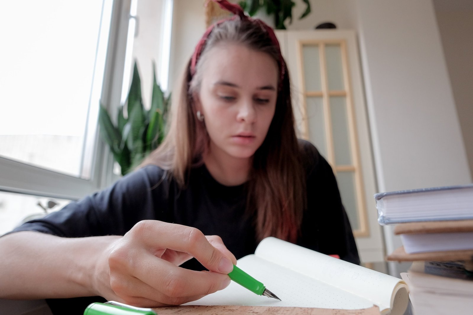 Estudiante preparándose de manera integral para la PAU, sentada en su escritorio con libros y cuadernos, tomando apuntes con una pluma verde en un entorno tranquilo y luminoso.