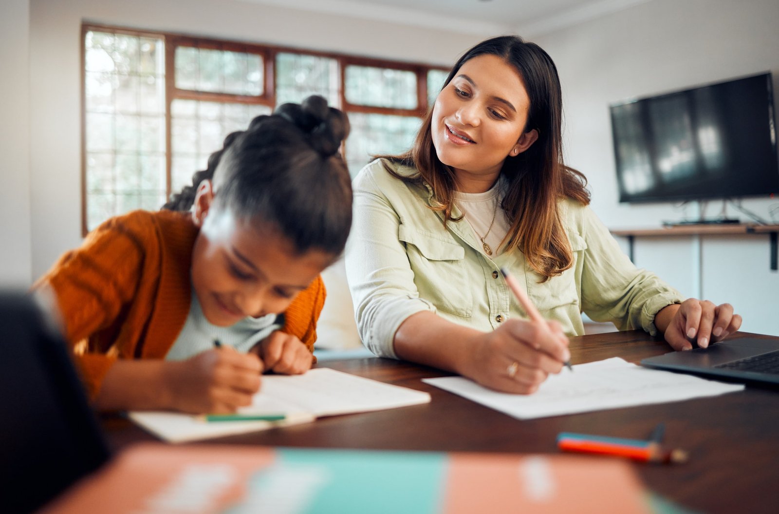 Una niña realiza tareas escolares junto a una mujer que supervisa y la apoya, representando un proceso de seguimiento personalizado en el entorno educativo para mejorar el rendimiento académico.